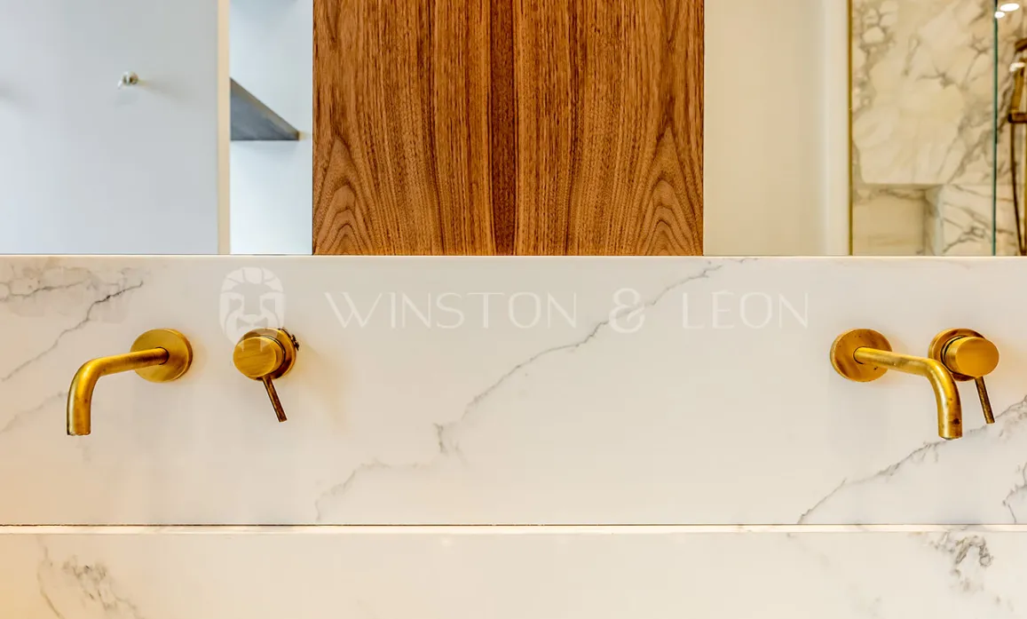 Luxury bathroom: brass wall-mounted faucets on veined white marble. Elegant contemporary design. Winston & Leon.