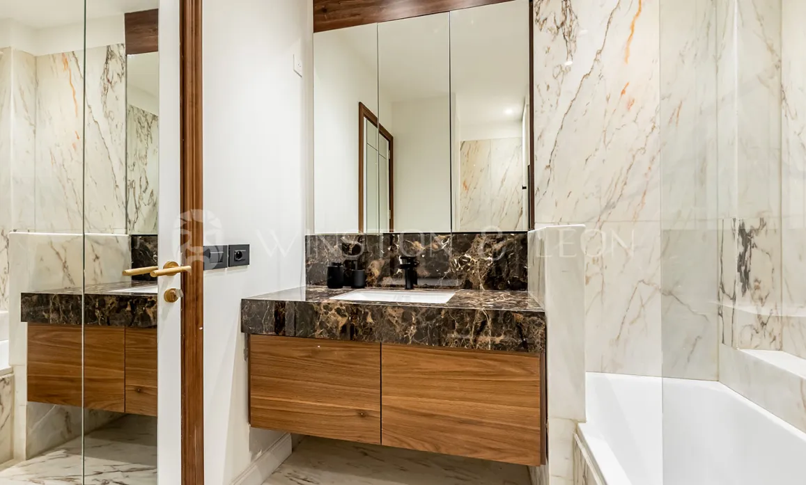 Modern luxury bathroom. Light and dark veined marble, elegant wooden vanity, and large mirror. High-end interior design.