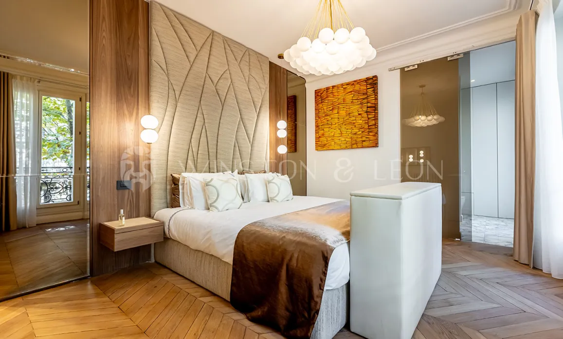 Modern luxury bedroom featuring upholstered headboard, chevron parquet, designer lighting, and artistic accents. Parisian elegance.