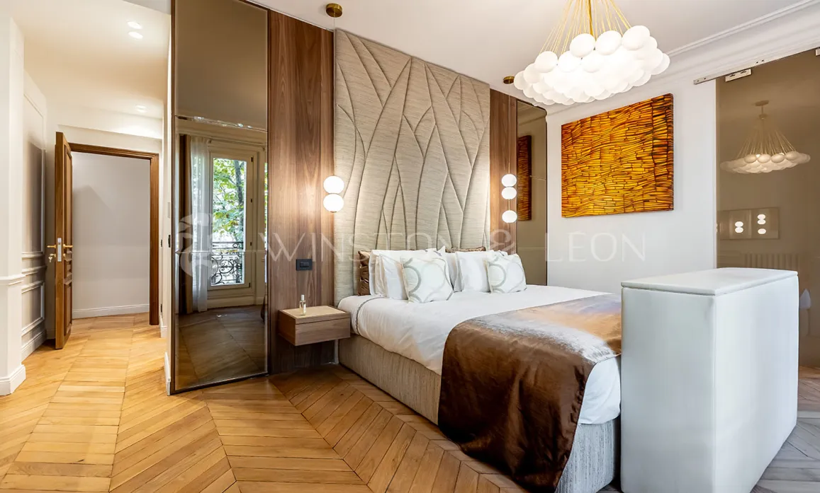 Modern luxury master bedroom: designer headboard, chevron parquet, elegant wood paneling, contemporary lighting. Refined ambiance & premium comfort.