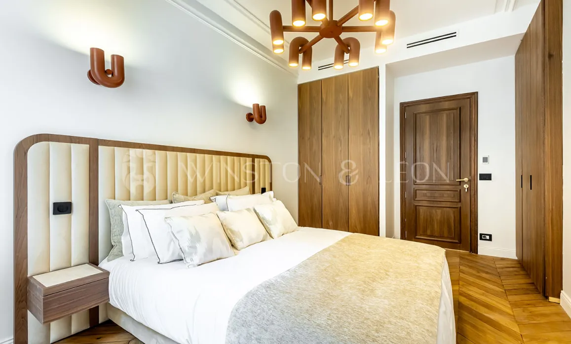 Modern luxury bedroom featuring padded headboard, designer lighting, built-in wardrobe, and parquet floor. Elegance & comfort.