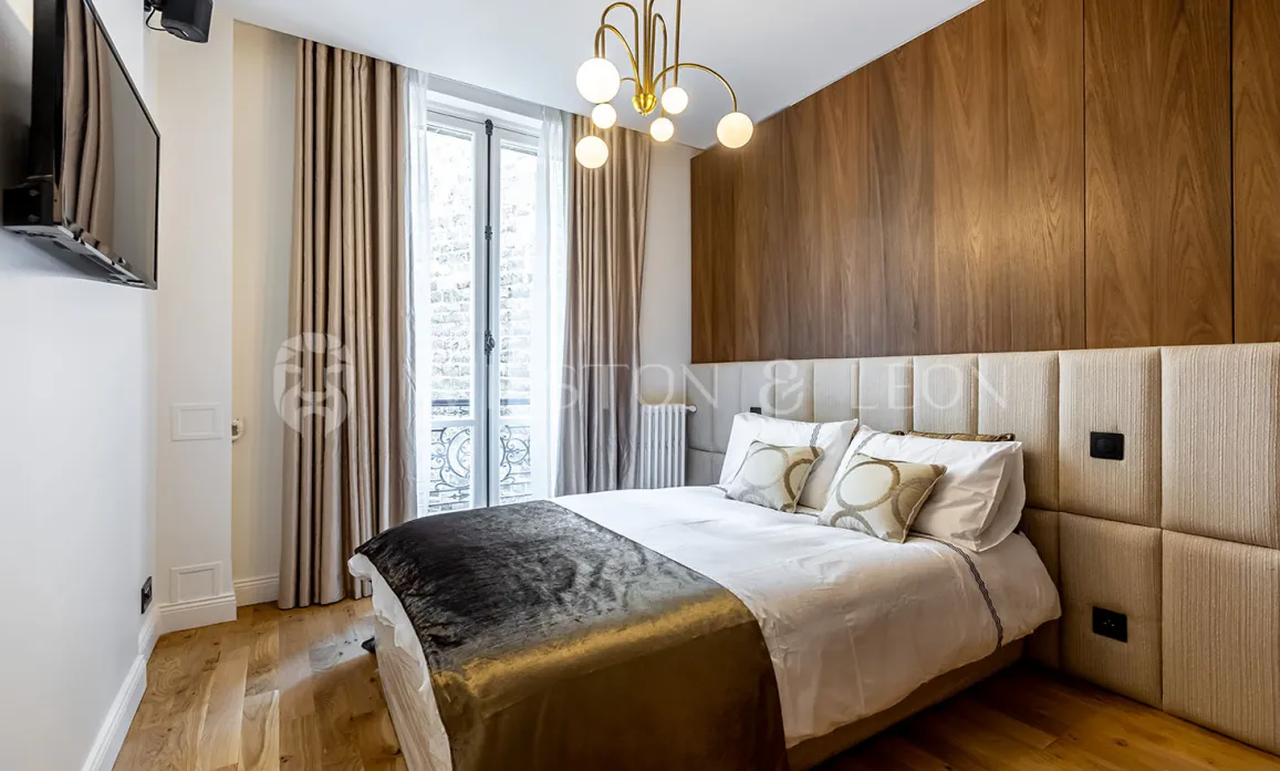 Modern luxury bedroom featuring wood paneling, padded headboard, and elegant chandelier. Contemporary design and comfort for a Parisian apartment.