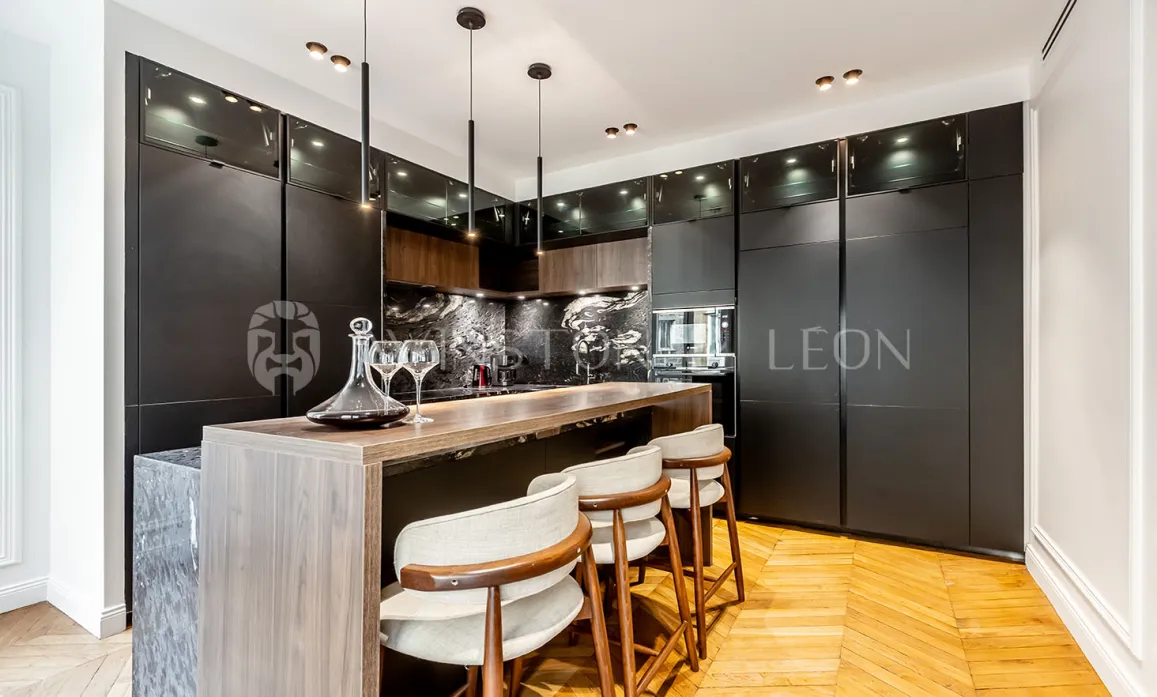 Contemporary luxury kitchen featuring a bar island, matte black finishes, light wood, marble, and parquet. Elegant & functional.