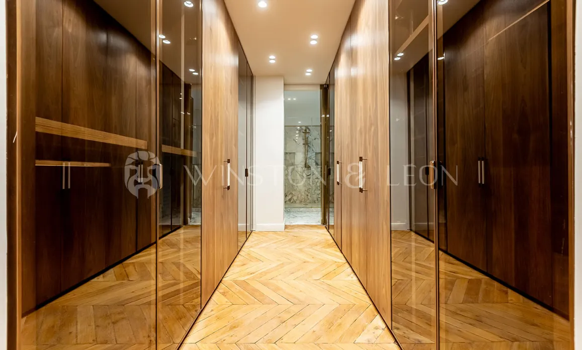 Modern luxury dressing room with wood and glass cabinets, herringbone parquet. Elegant storage for high-end property.