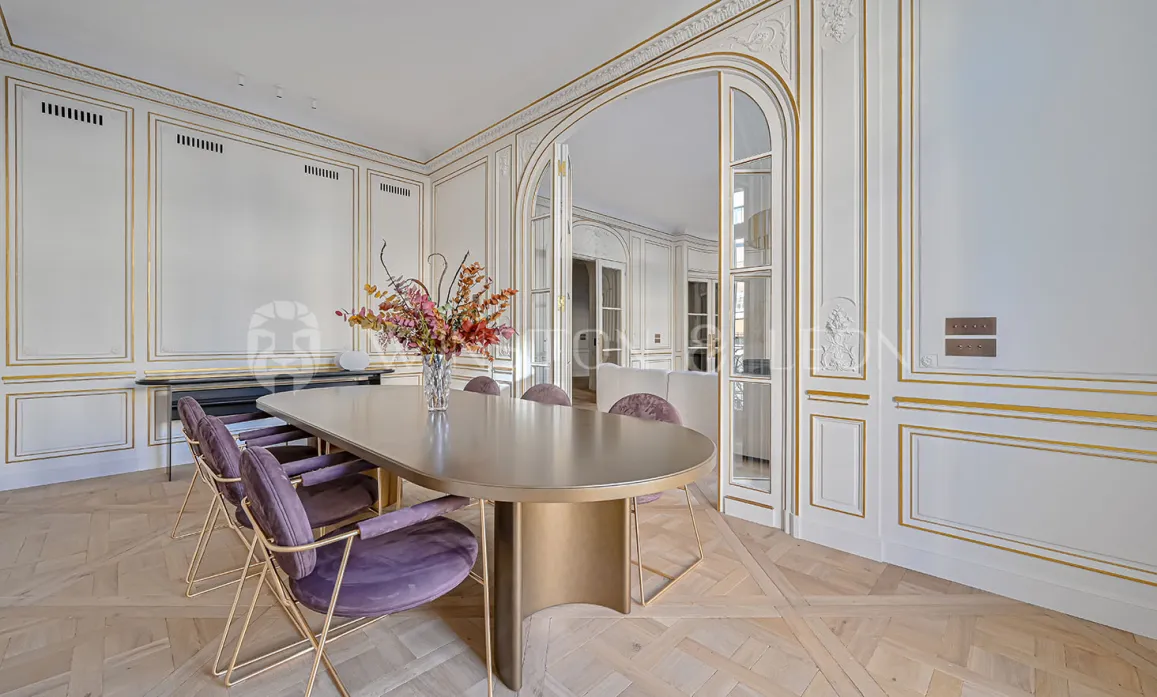 Elegant luxury Parisian dining room. Gilded moldings, parquet flooring, modern design table, velvet chairs. Haussmannian refinement.