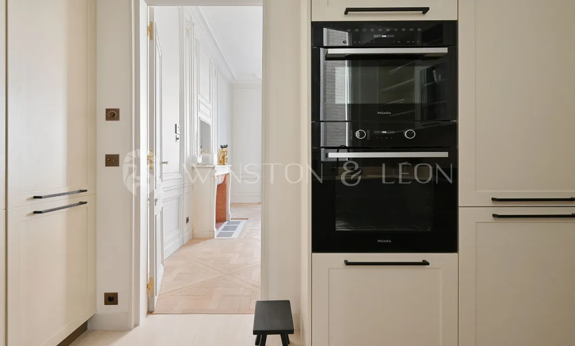 Modern Miele kitchen with integrated appliances, overlooking an elegant Haussmannian living room. Luxury apartment Paris.