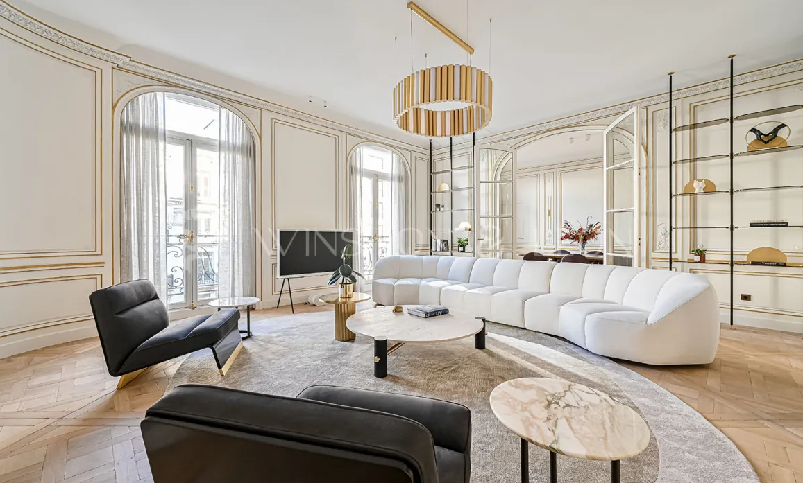 Exceptional Parisian Haussmannian living room: gold moldings, herringbone parquet, white designer sofa, luxury furniture, natural light.