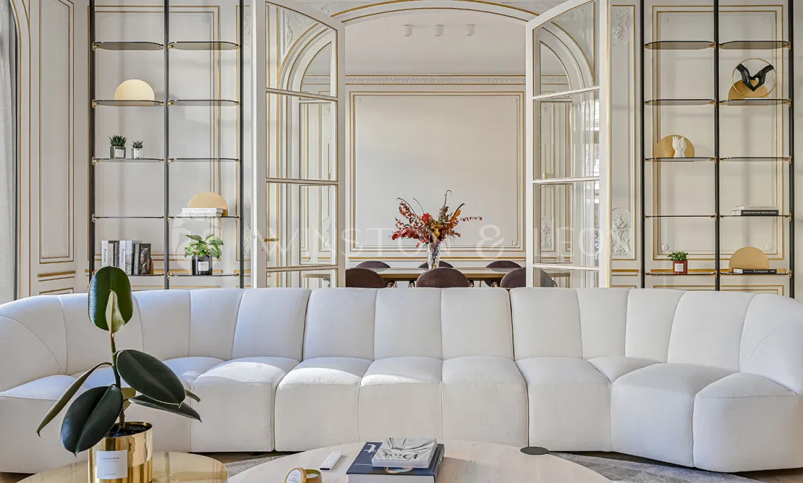 Elegant luxury living room, modern white sofa, gold moldings. Chic and refined ambiance for an exceptional Haussmannian apartment.