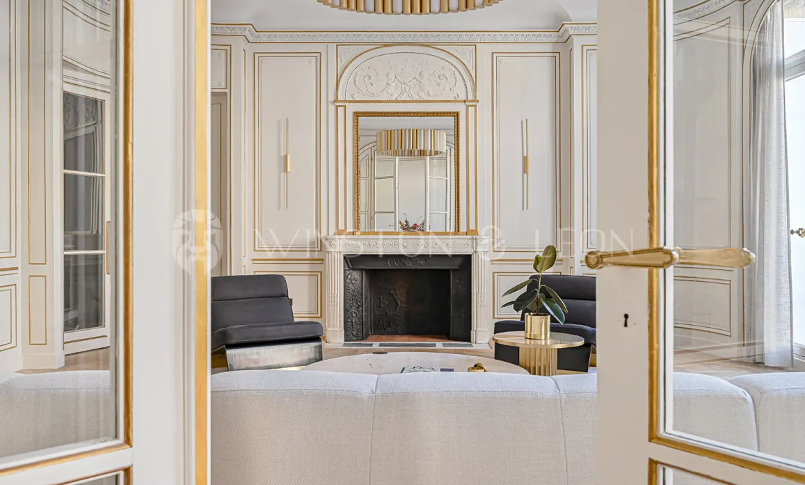 Luxury Parisian living room: ornate gold paneling, classic fireplace, and elegant modern furnishings. A prestigious interior blending old charm & modern design.