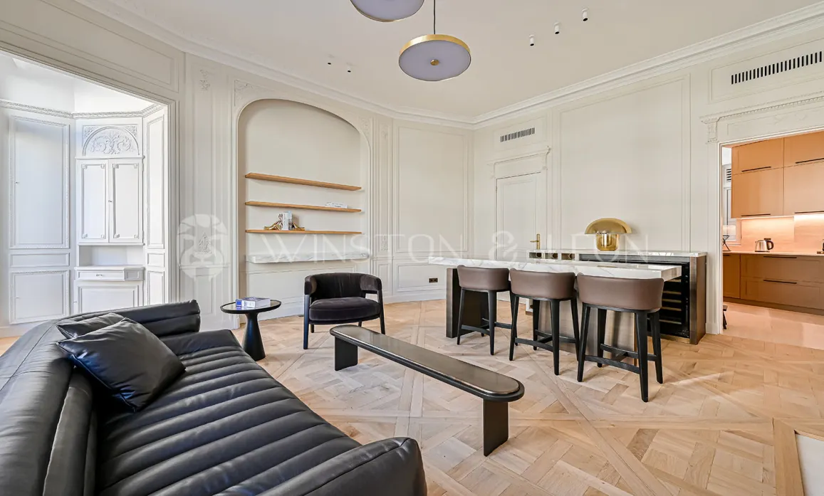 Stunning luxury Parisian living room. Contemporary design, Versailles parquet, elegant moldings, integrated bar & modern kitchen. Refined, bright ambiance.
