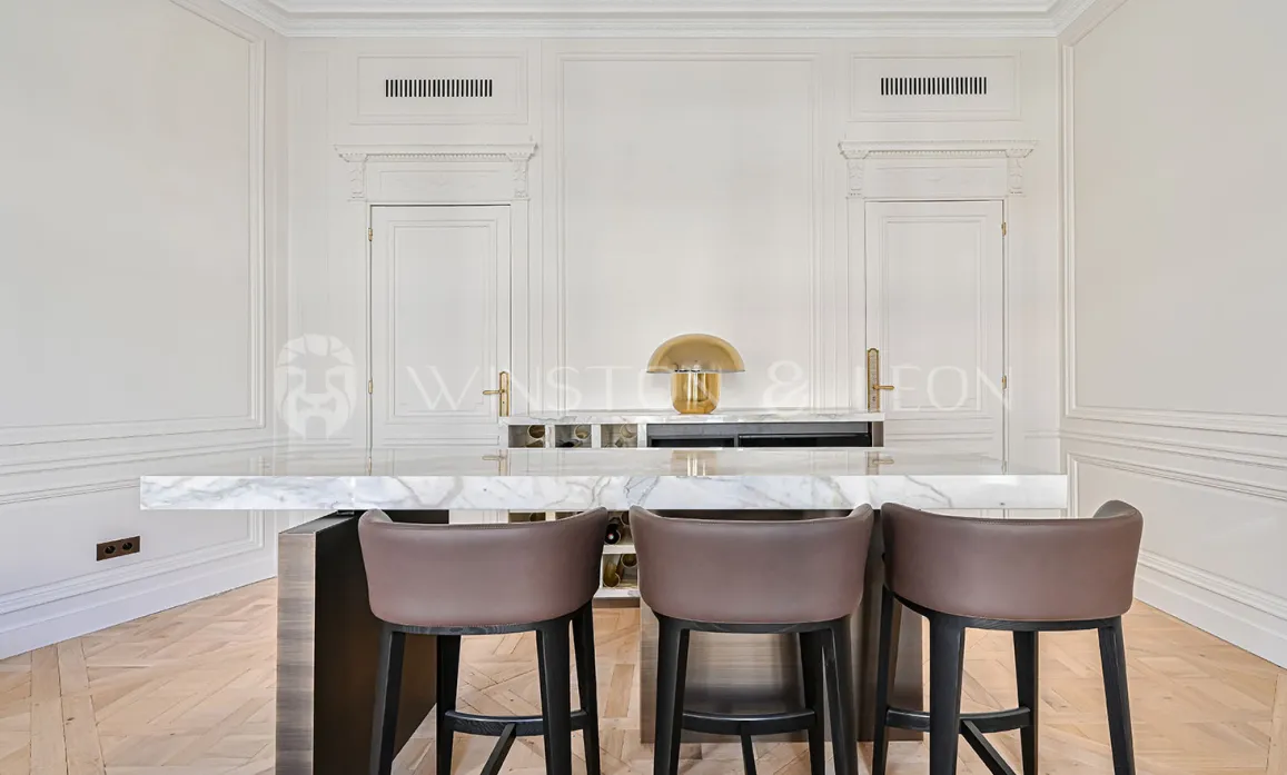 Luxury kitchen with marble island, designer stools. Elegant paneling, gold lamp. Prestige interior, chic Parisian apartment.