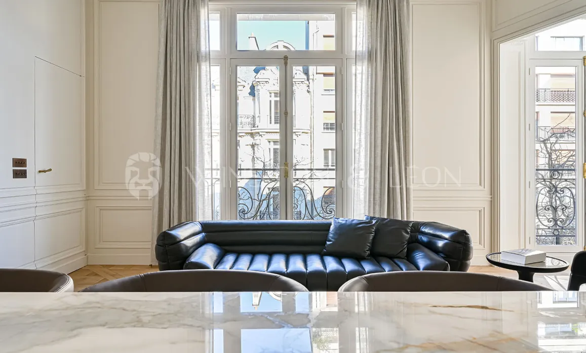 Luxury Parisian living room with black leather sofa, elegant moldings, and Haussmannian view. Contemporary design and refinement.