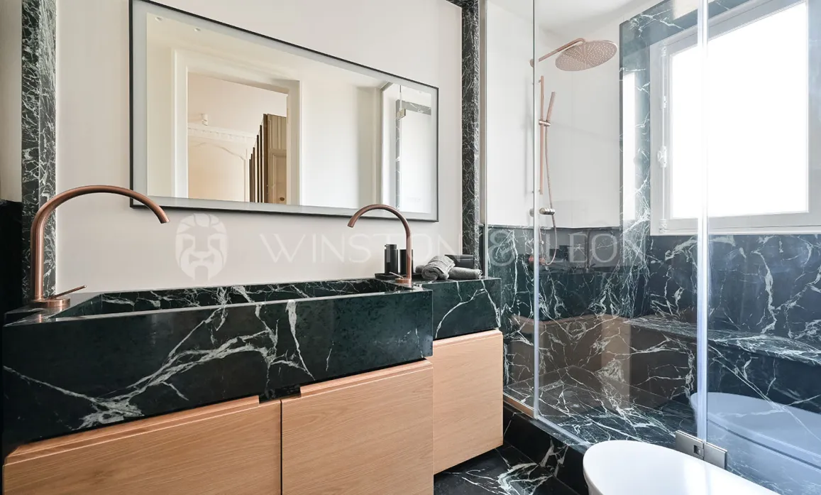 Luxury bathroom. Black veined marble, light wood double vanity, copper fixtures. Modern walk-in shower. Elegance and sophistication.