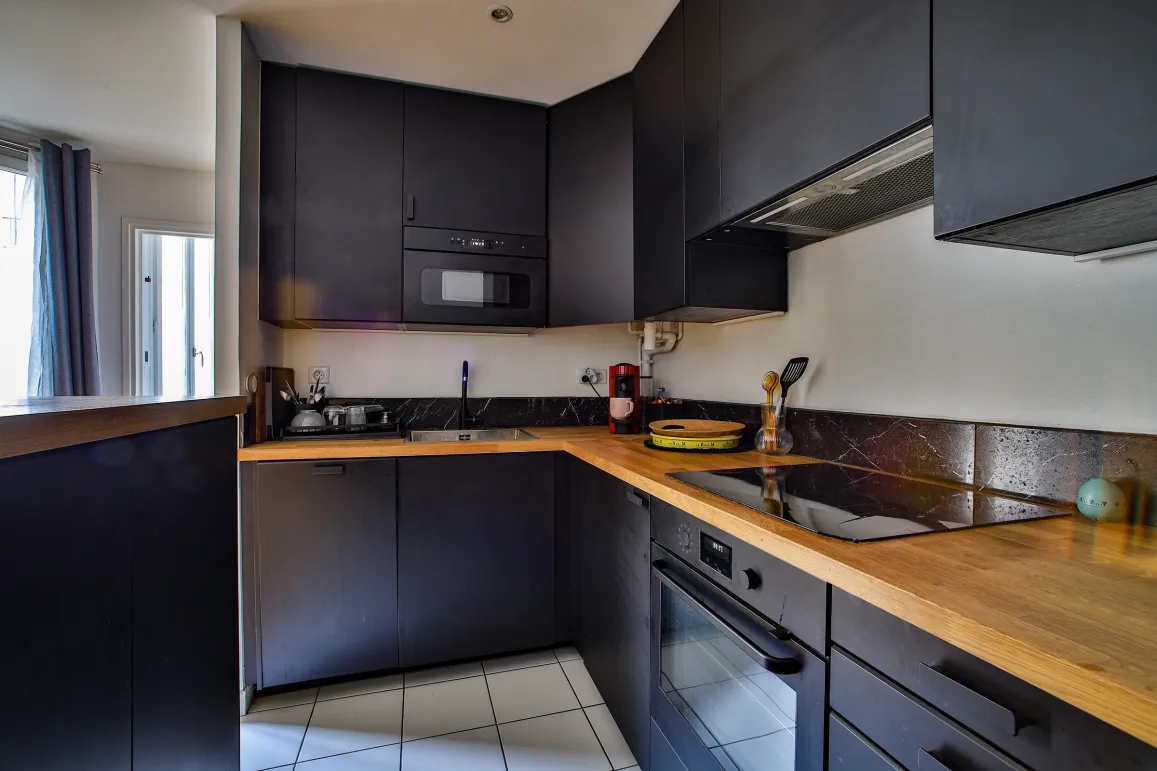 High-end kitchen, matte black cabinetry, wood countertop. Integrated appliances. Modern and luxurious ambiance.