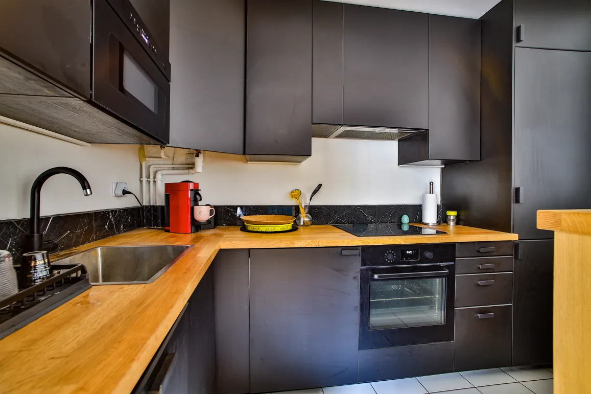 Luxury modern kitchen: matte black cabinets, light wood countertop, fully equipped. Elegant contemporary design.