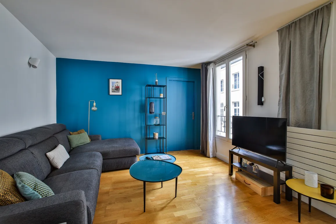 Bright modern living room with vibrant blue accent wall, grey sectional sofa, elegant hardwood floors. Perfect for a luxury apartment.