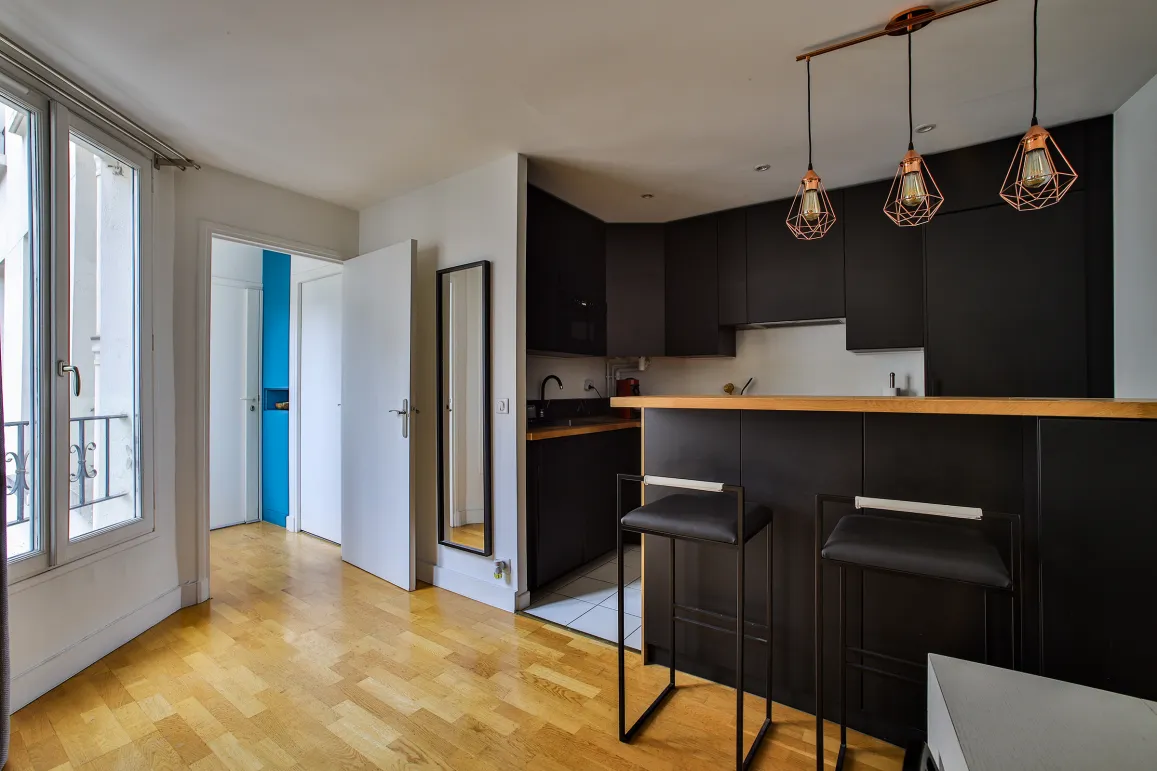 Modern black kitchen with bar, design stools, hardwood floor & copper lights. A bright and elegant living space.