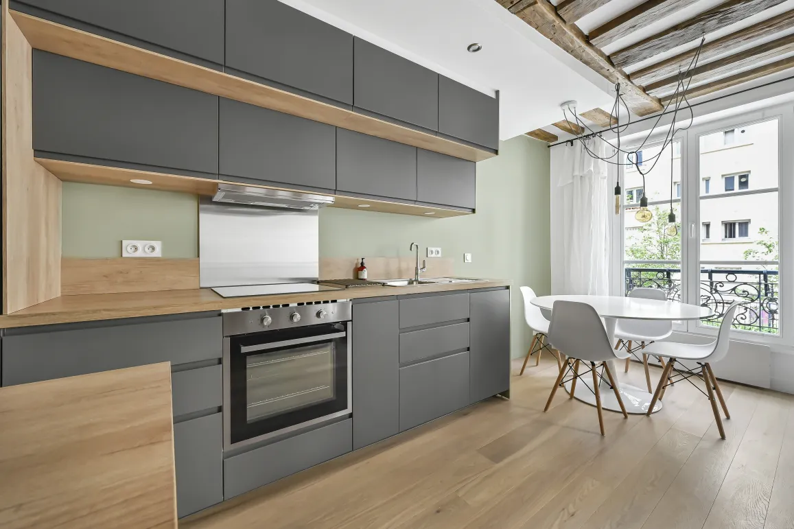 Modern anthracite grey and light wood kitchen. Sleek design, exposed beams, city view. Bright luxury apartment.