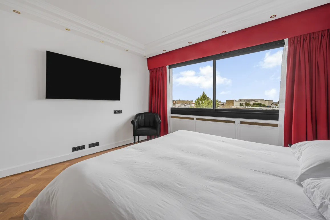 Bright, modern master suite with city views, TV, armchair, and hardwood floor. The luxury and comfort of a high-end apartment.
