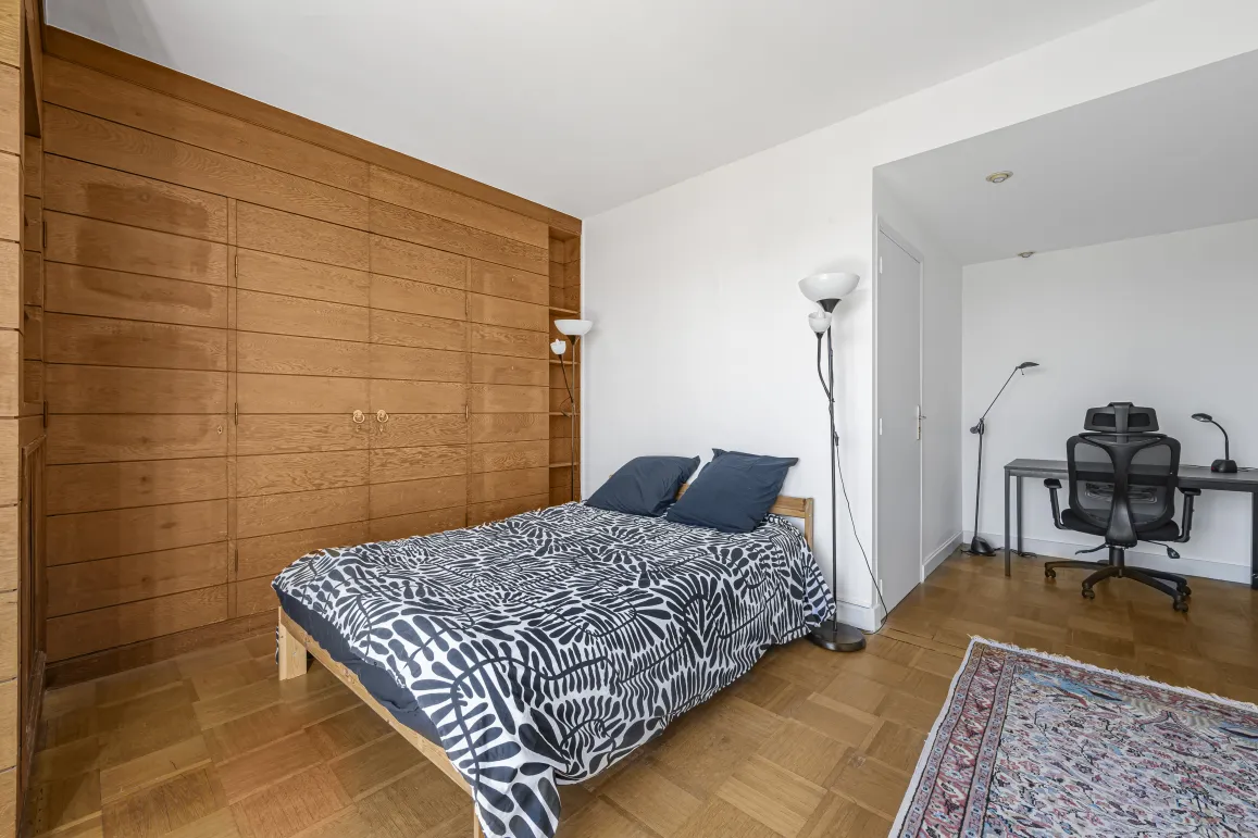 Elegant bedroom featuring a large built-in wooden wardrobe, parquet flooring, and a discreet office area. Comfort and style for luxury living.