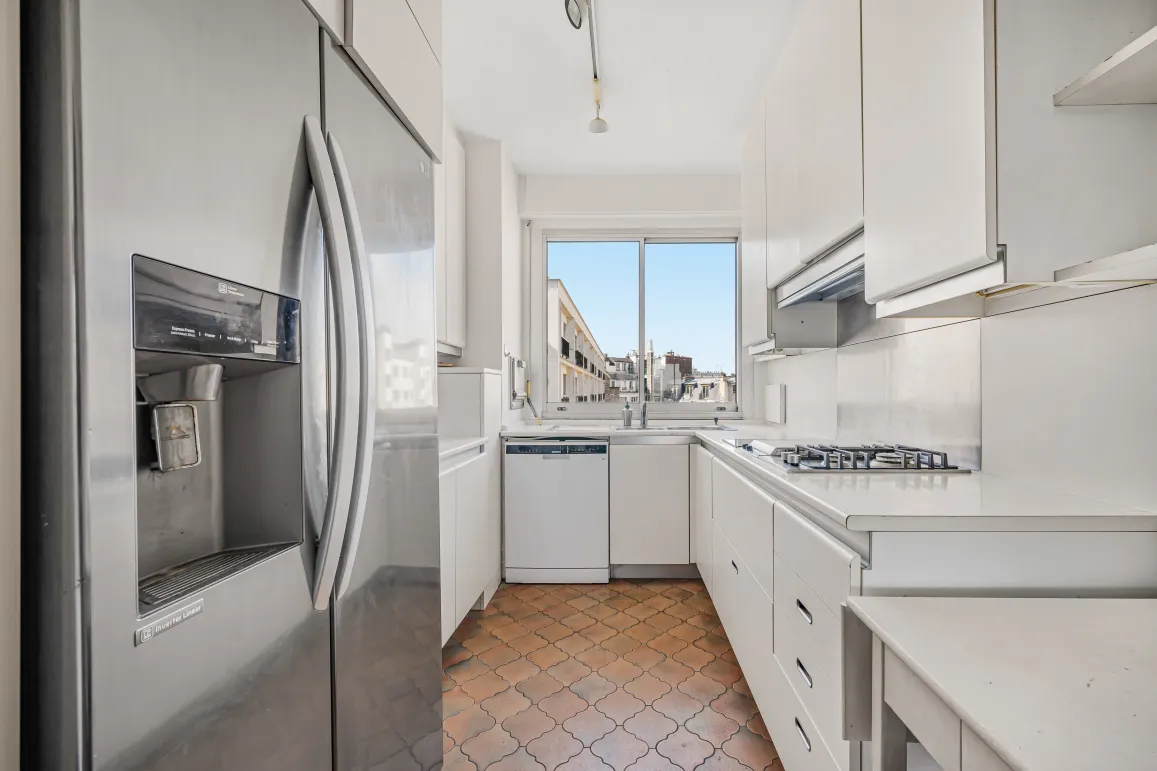 Contemporary white kitchen, fully equipped with American fridge, gas hob, and beautiful city view. Luxury and functionality.
