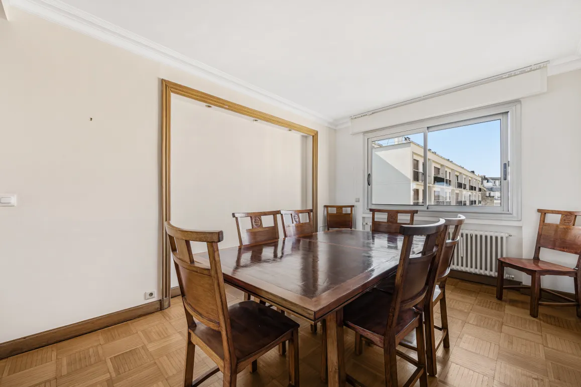 Spacious, bright dining room with parquet flooring, large solid wood table, and urban views. Perfect for a luxury apartment.