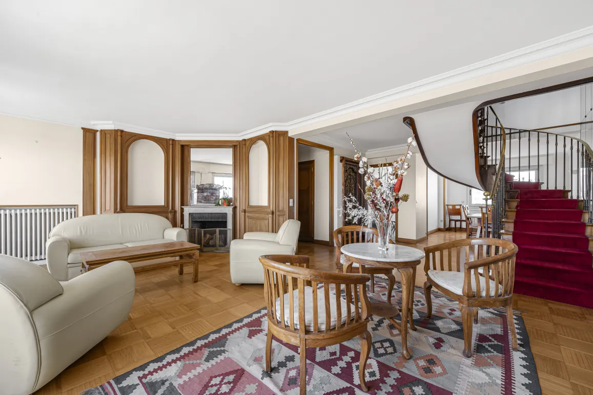 Elegant luxury living room with fireplace, wood paneling, parquet flooring, and majestic spiral staircase. Spacious property.