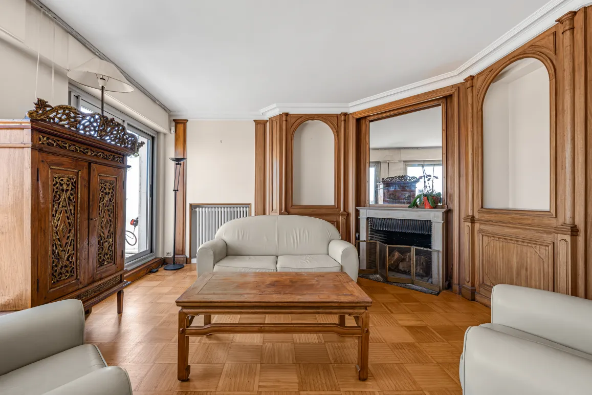 Luxury living room featuring ornate wood paneling, parquet flooring, fireplace, and classic furniture. Timeless elegance for an exceptional apartment.