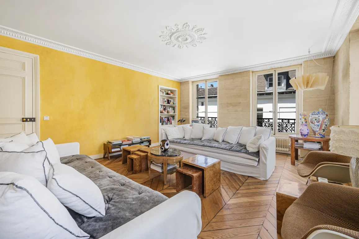 Bright luxury living room with textured yellow wall, parquet, moldings & white sofas. Parisian elegance.