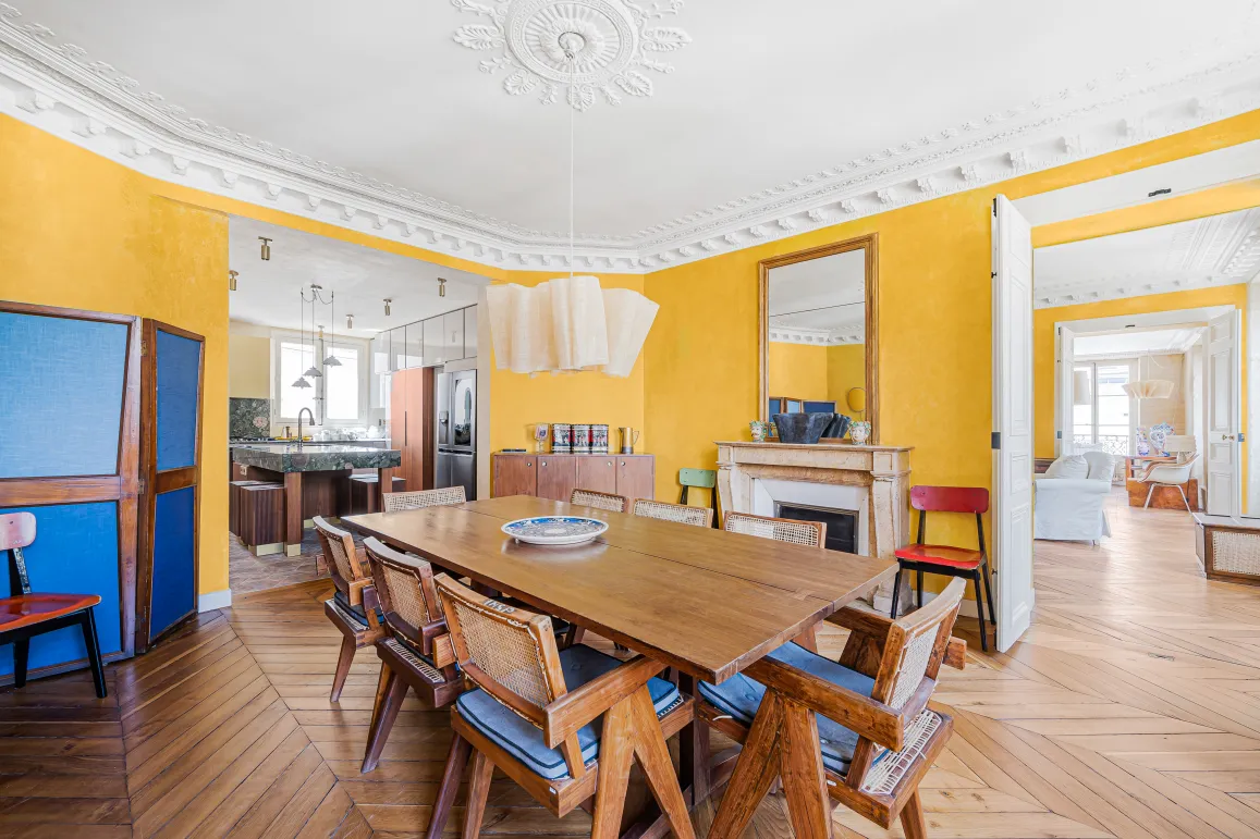 Elegant Parisian dining room with yellow walls, herringbone parquet, fireplace. Renovated luxury apartment, blending old charm & modern design.