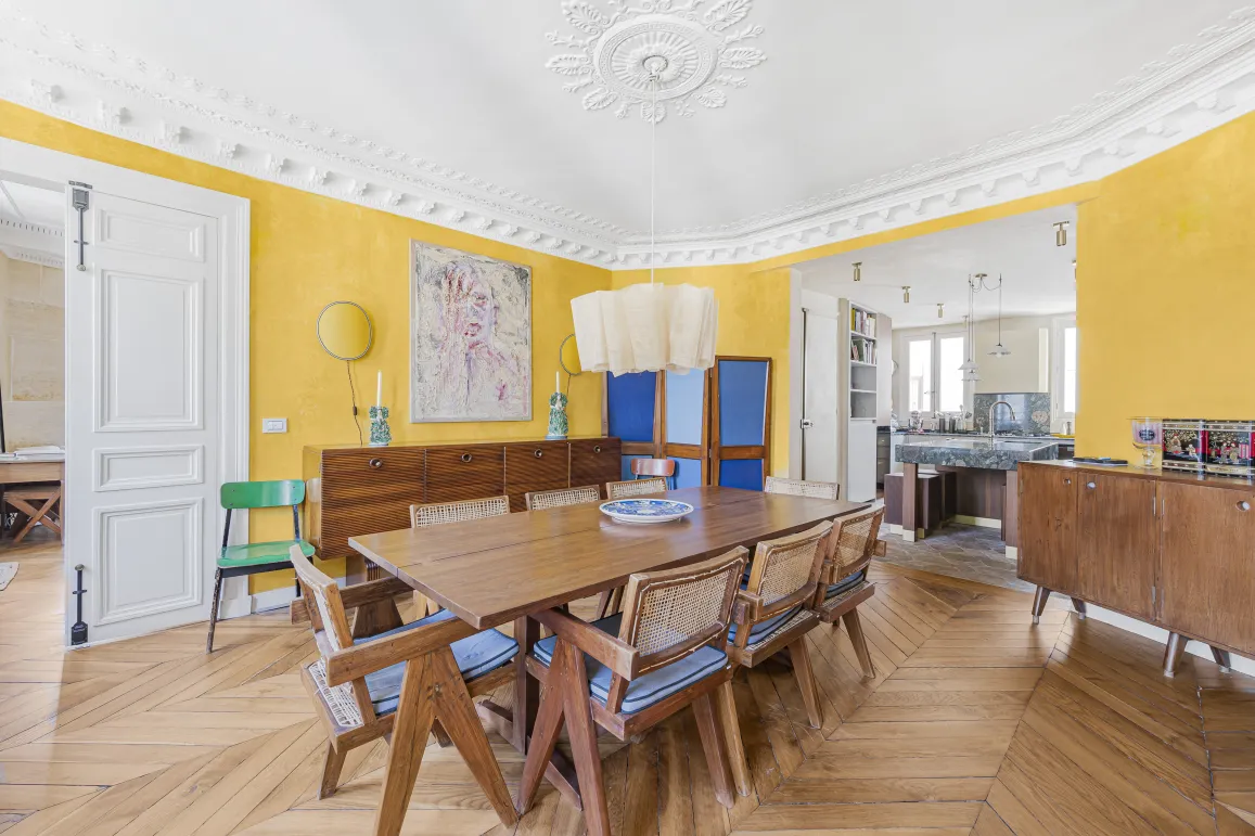 Luxury Parisian apartment: bright dining room with yellow walls, herringbone parquet, moldings. Design open kitchen. Vibrant elegance.