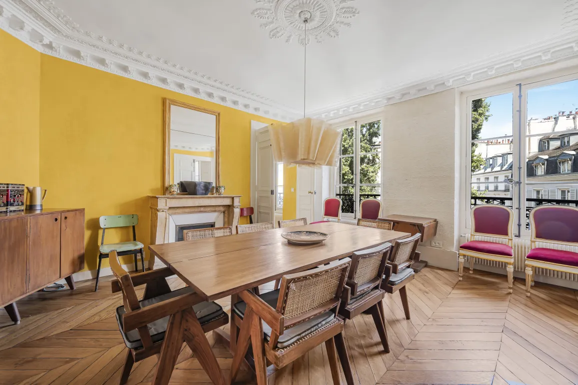 Luxury Parisian apartment: bright dining room with parquet, moldings, fireplace, and city view. Haussmannian elegance.