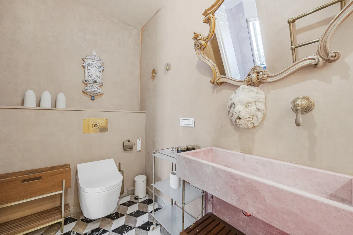 Luxury bathroom with pink marble sink, gold mirror, designer toilet and geometric tiles. Elegant and refined ambiance.