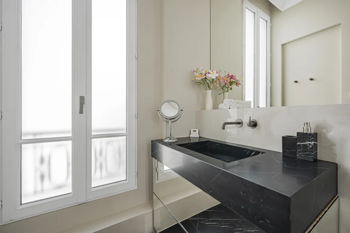 Luxury bathroom featuring black marble vanity and modern design. Elegant, refined ambiance with a bright window.