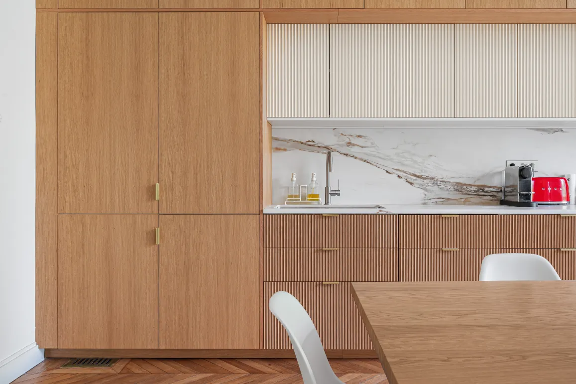 Luxury modern kitchen: light wood, veined marble, gold finishes. Contemporary design with herringbone parquet and Smeg appliance.