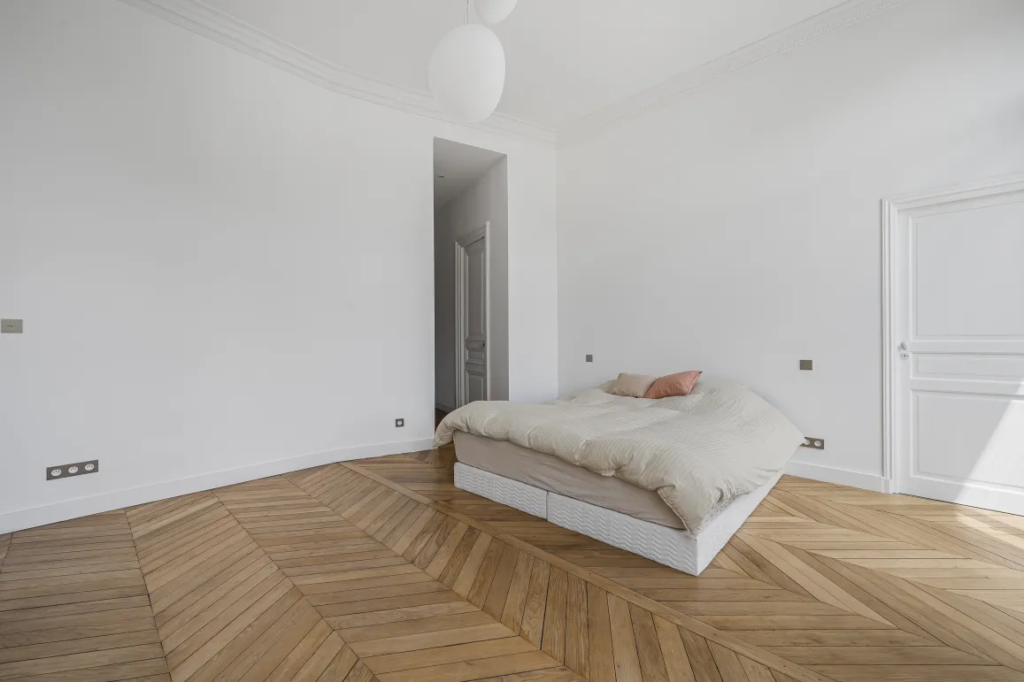 Luxury minimalist bedroom, chevron parquet, white walls. Parisian elegance, natural light. Ideal Haussmannian apartment.