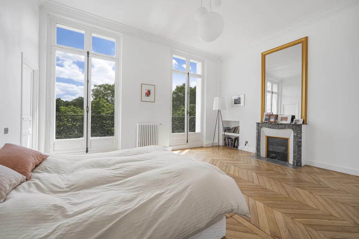 Luxurious bright bedroom with stunning green views. Herringbone parquet, fireplace and gilded mirror. Elegance and comfort.