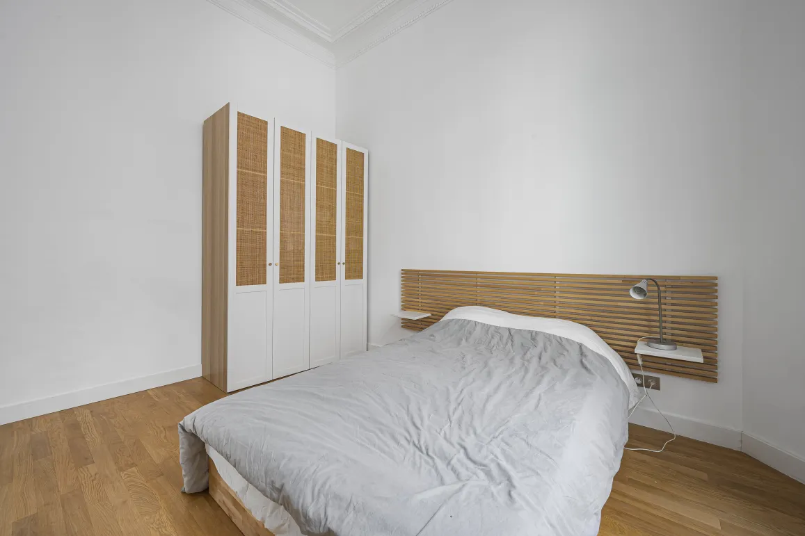 Modern, bright bedroom featuring wood flooring, designer slatted headboard, and elegant rattan wardrobe. Perfect for luxury apartment.