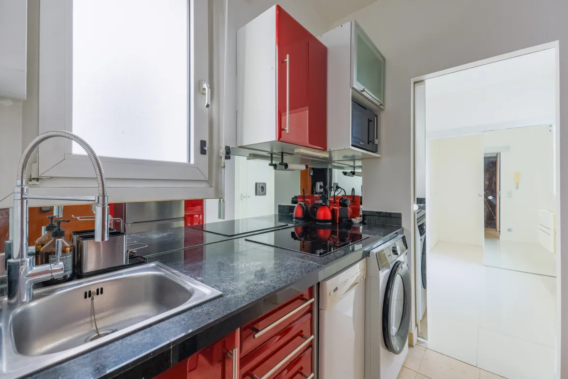 Sleek compact kitchen with red gloss cabinets, black granite, integrated appliances. Perfect for modern urban apartments.