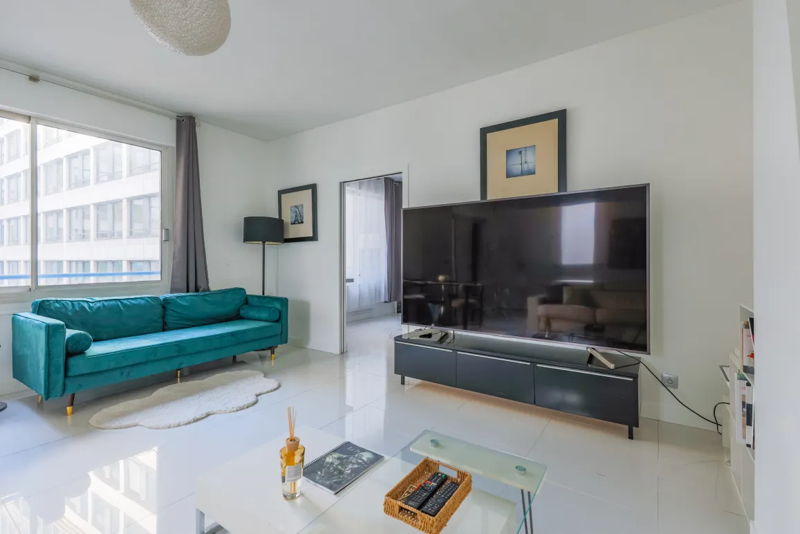Bright, modern living room featuring a teal velvet sofa, large TV, and sleek design. Perfect for a luxury urban apartment. Comfort and style.
