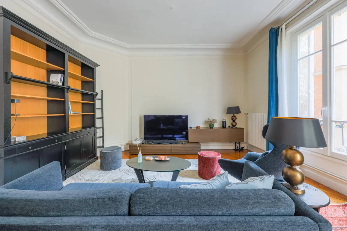 Elegant Parisian luxury living room with built-in bookshelf, designer sofa & TV. Bright and modern apartment space.