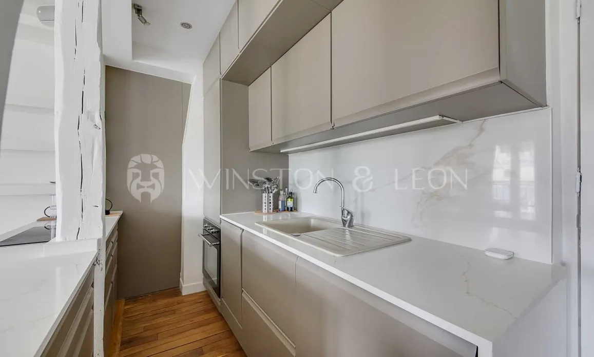 Modern, elegant kitchen with light grey cabinets, marble countertop & backsplash. Luxurious design for Parisian apartment.