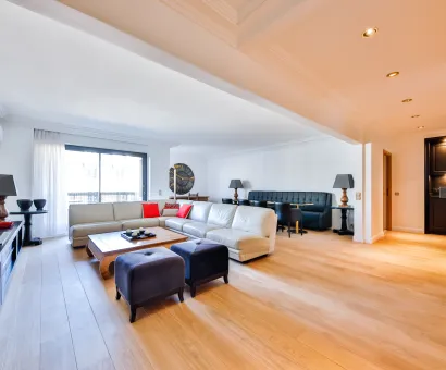 Spacious, bright luxury living room with light wood floors, modern sectional sofa, dining area, and integrated bar. High-end contemporary design.