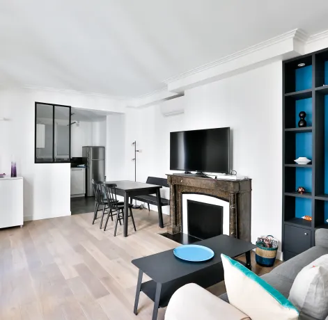 Bright modern living room with open kitchen, fireplace, and vibrant blue built-in shelving. Luxury apartment design.
