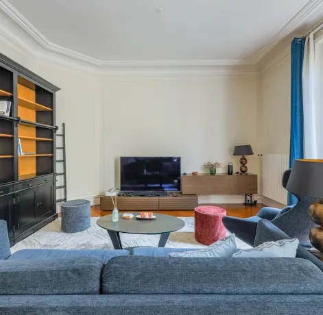 Elegant Parisian luxury living room with built-in bookshelf, designer sofa & TV. Bright and modern apartment space.