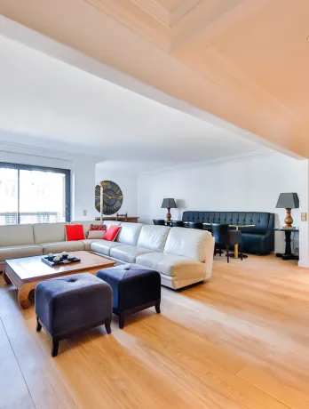 Spacious, bright luxury living room with light wood floors, modern sectional sofa, dining area, and integrated bar. High-end contemporary design.