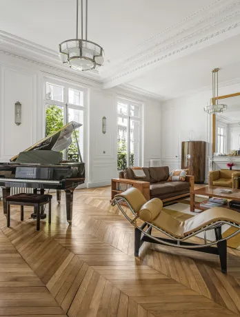 Luxury Parisian living room with grand piano, herringbone parquet, moldings & green views. Timeless elegance & design.