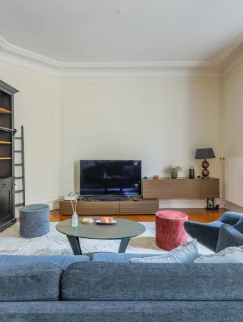 Elegant Parisian luxury living room with built-in bookshelf, designer sofa & TV. Bright and modern apartment space.